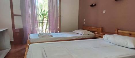 Una habitación con dos camas de madera, una ventana con cortinas y una puerta.