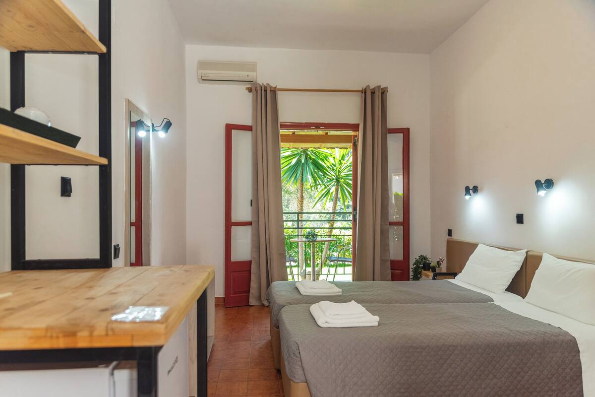 Una habitación de hotel con dos camas, una mesa de madera, un espejo y vistas a zonas verdes.