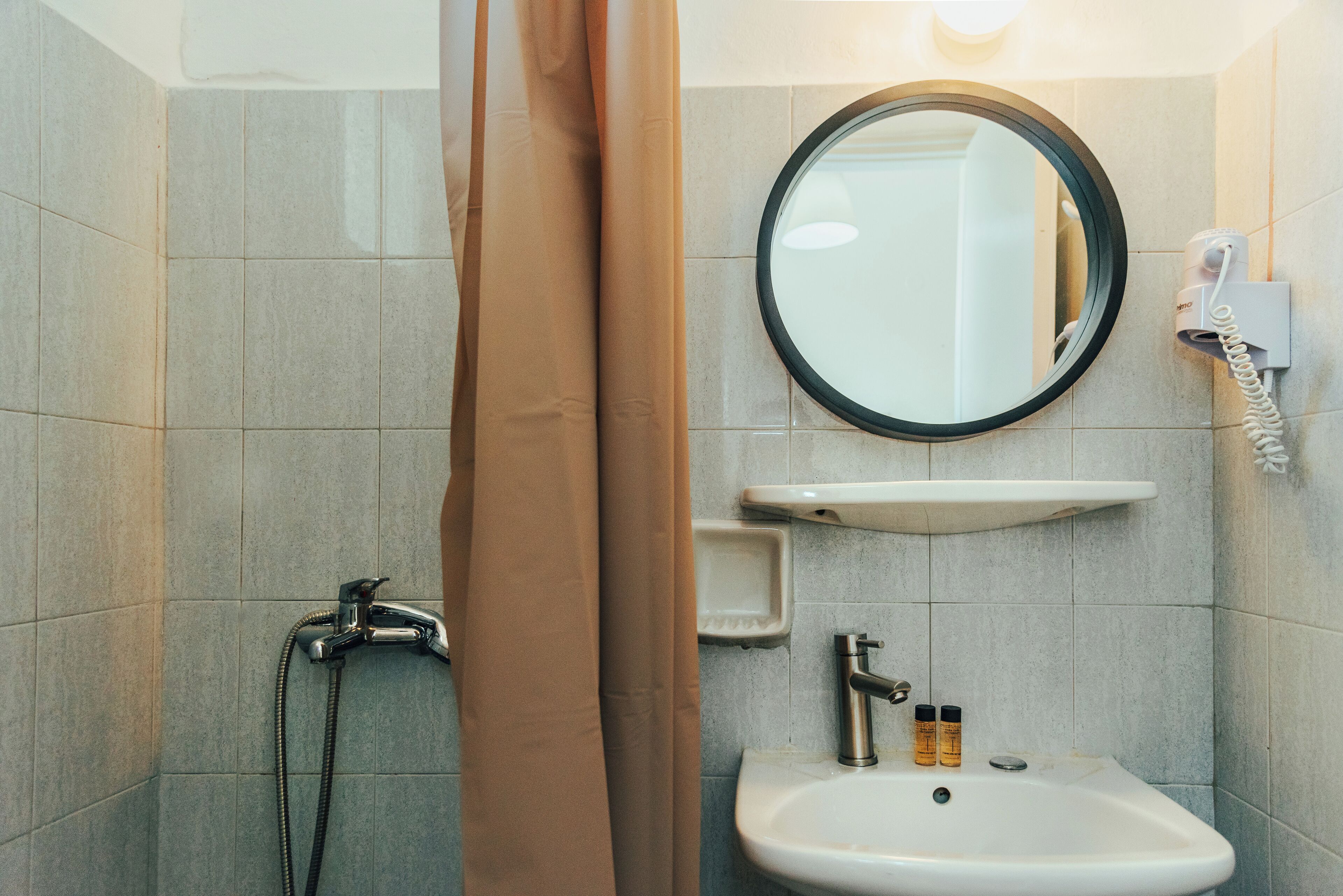 A bathroom with a shower, a sink, a mirror, and a hairdryer mounted on the wall.