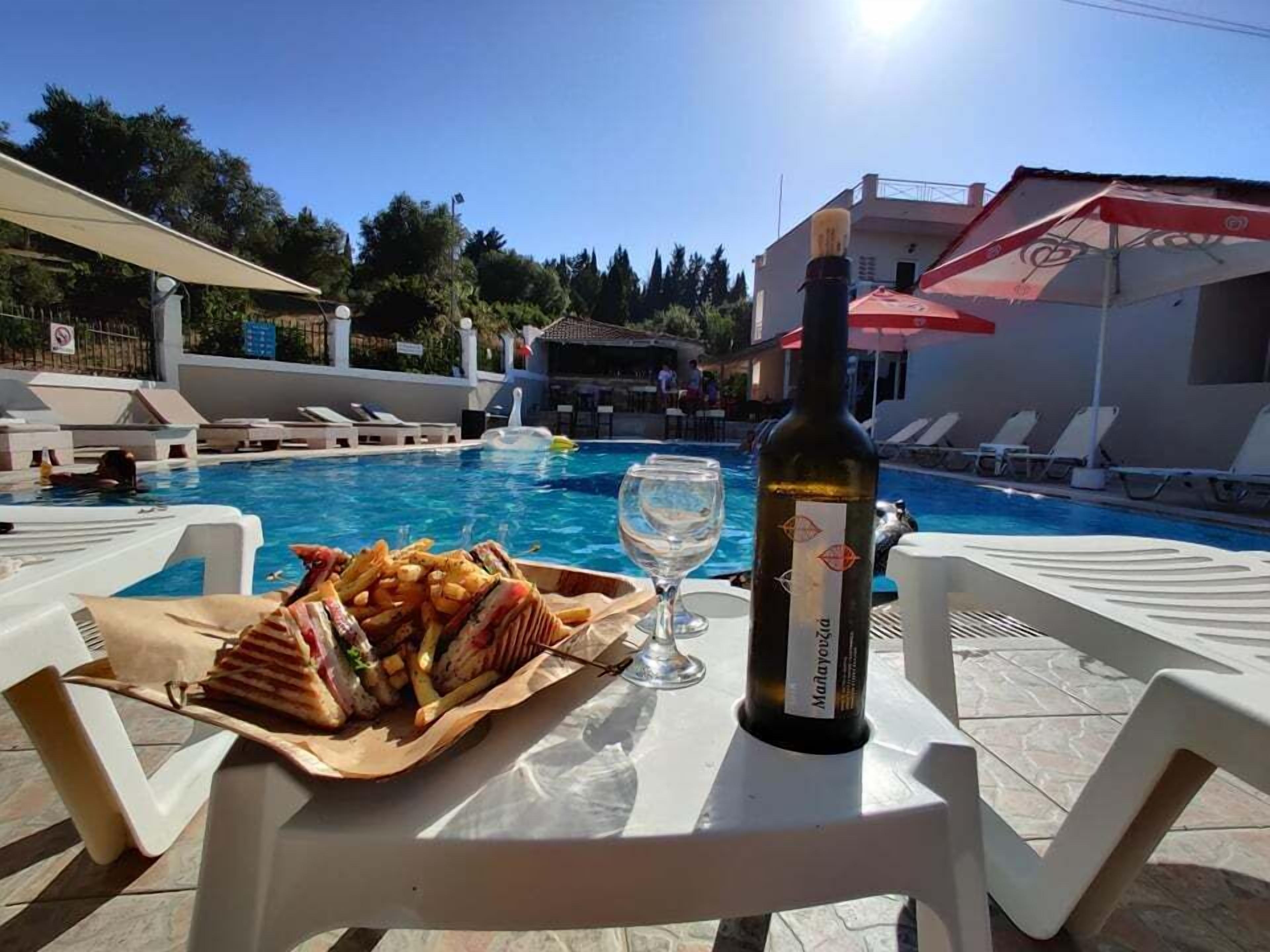 Una mesa junto a la piscina con una botella de vino, una copa y una bandeja de comida.