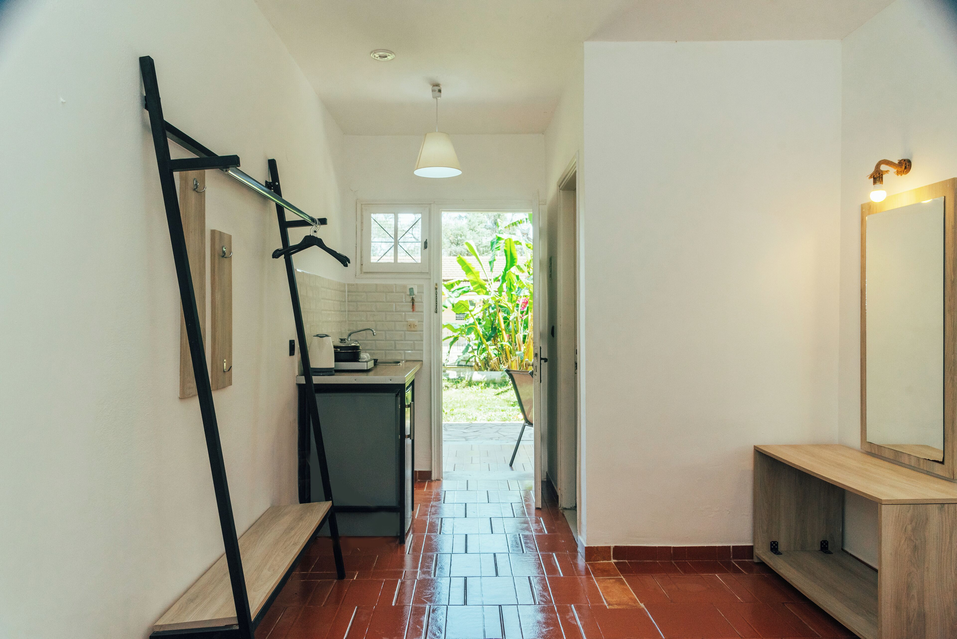 A narrow hallway with a kitchen area on the left, a wooden bench, and a mirror on the right.