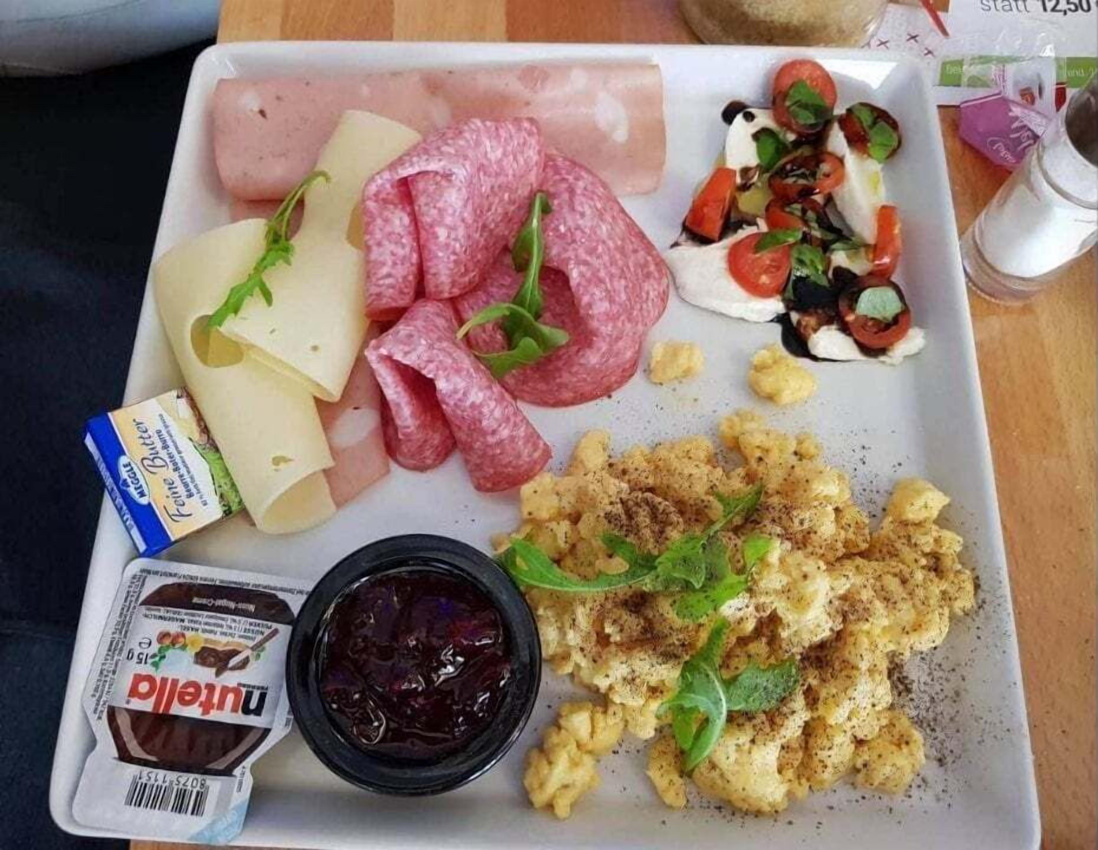 A meal tray with various foods including cheese, salami, a salad, scrambled eggs, and a container of jam.