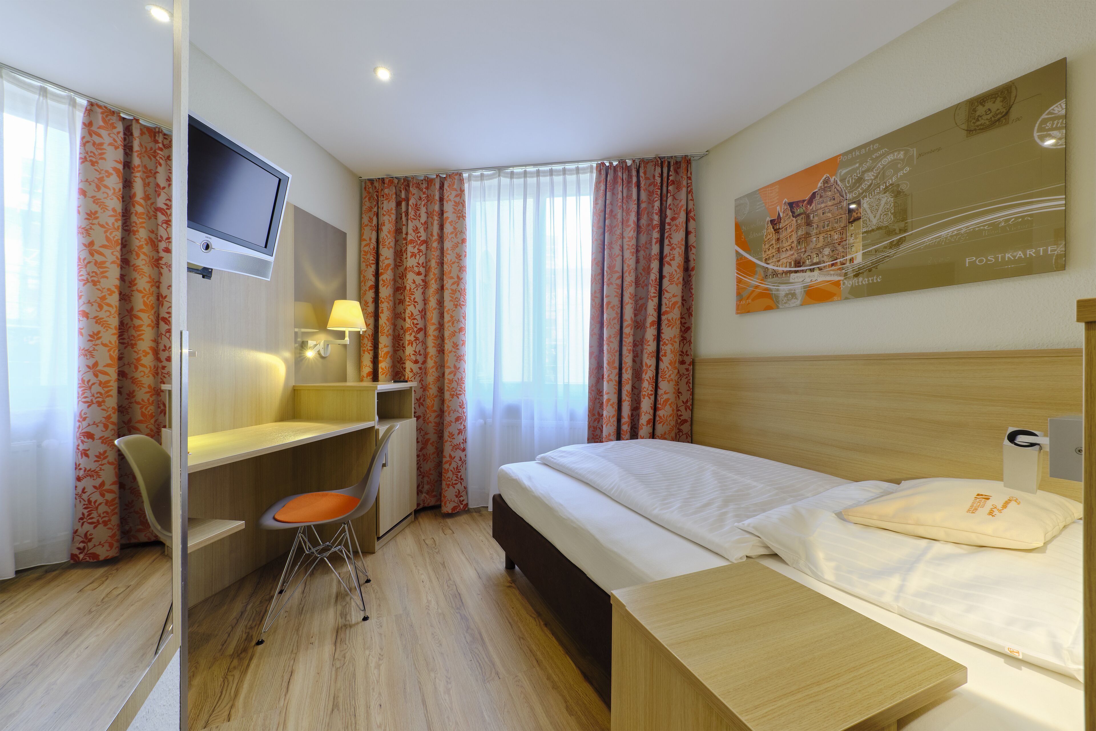 Habitación de hotel con cama, escritorio, silla, televisor y un cuadro en la pared.