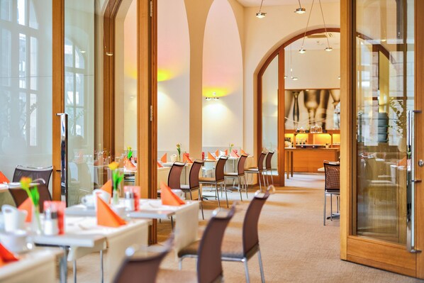 A modern dining area with high ceilings, large windows, and a warm color palette. - Hotel Victoria (Nuremberg)