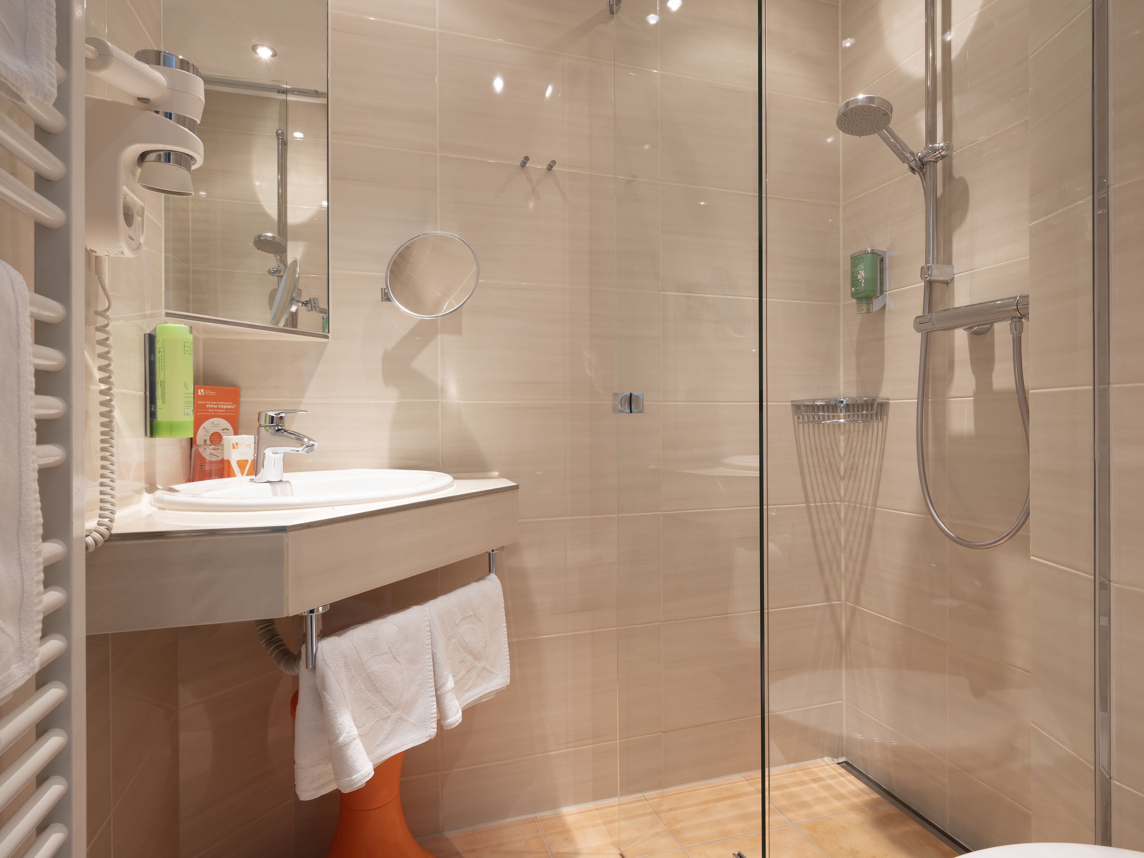 A modern bathroom with a glass-enclosed shower, a sink with a towel rack, and toiletries on the counter.