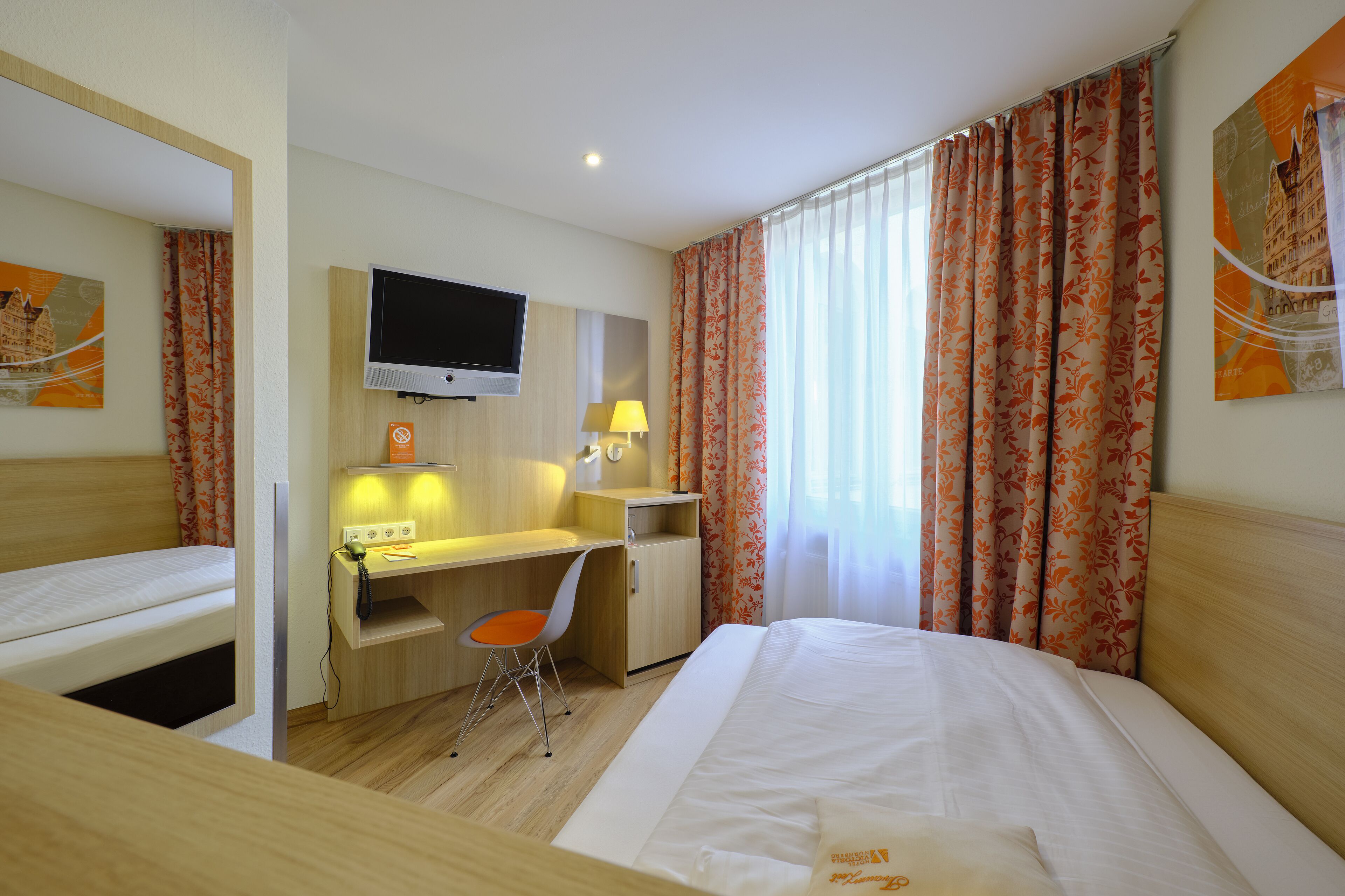 Una habitación de hotel con cama, escritorio, silla, televisor y ventana con cortinas.