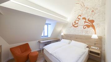 Et moderne soveværelse med ovenlys, en træsenggavl, en seng med hvide sengetøj, en orange lænestol og et skrivebord med en lampe.