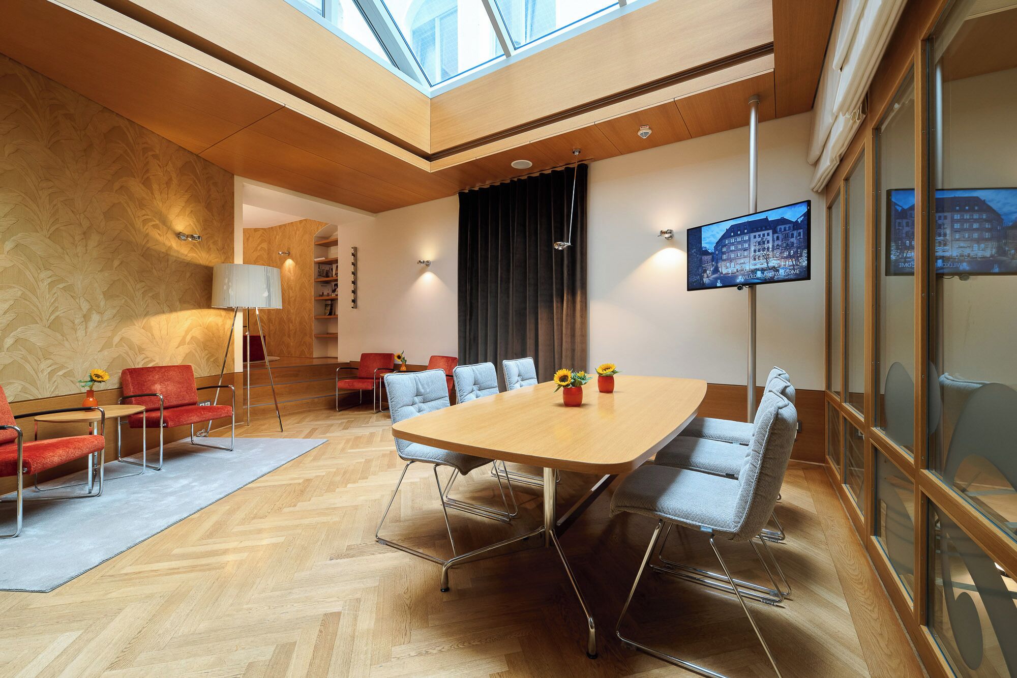 A modern conference room with a large table, comfortable seating, a TV, and a city view.