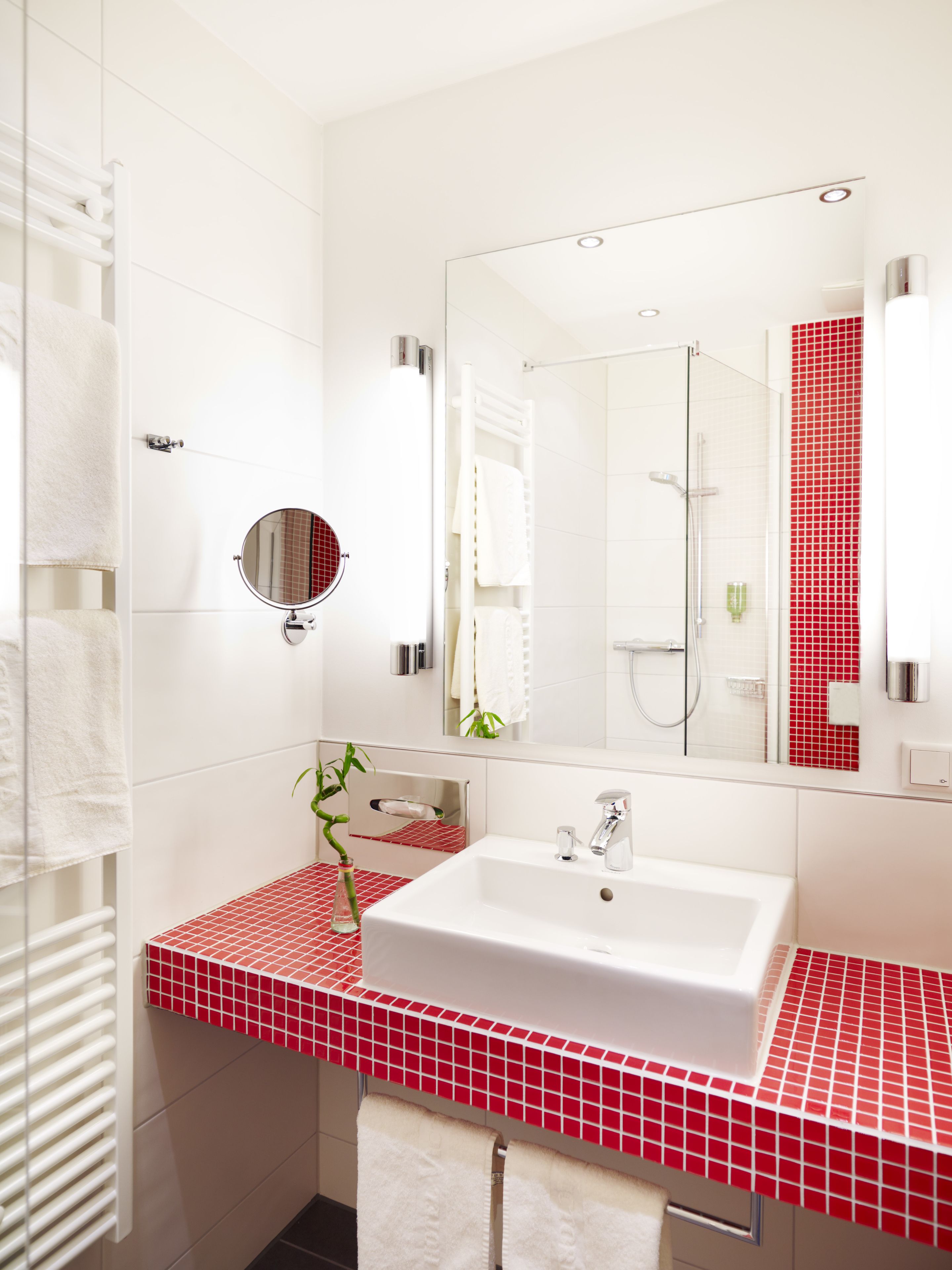 A modern bathroom with a white sink, red-tiled countertop, and a large mirror.