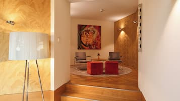 A modern interior with a wooden floor, a round coffee table, two armchairs, a large abstract painting, and a floor lamp.