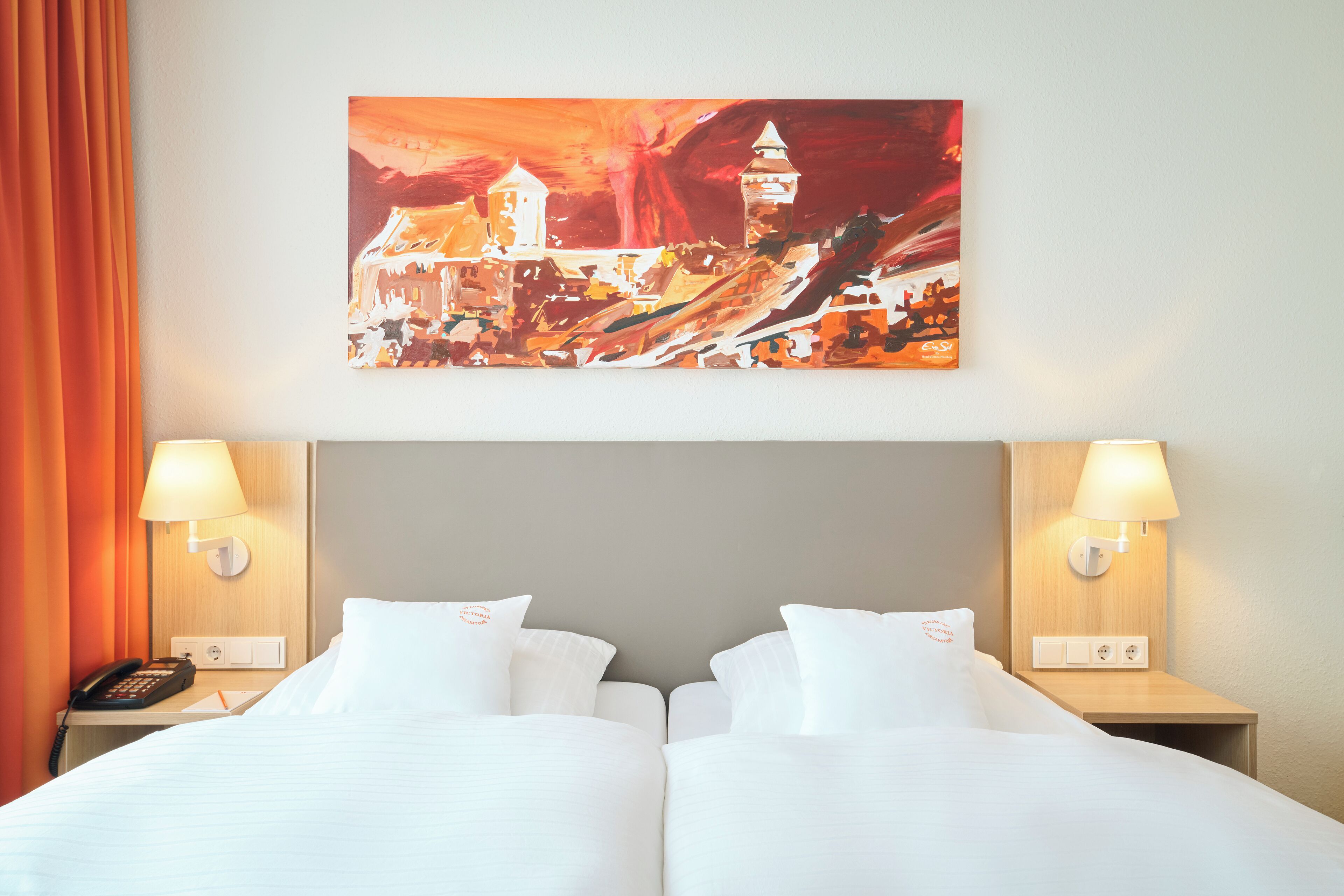 Ein Hotelzimmer mit zwei Betten, einem Bild an der Wand und zwei Nachttischlampen.
