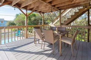 Une terrasse en bois avec une table et des chaises, un escalier et une piscine en arrière-plan.