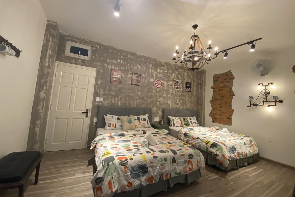 Quarto com duas camas, um candelabro, uma parede de tijolos e uma porta.