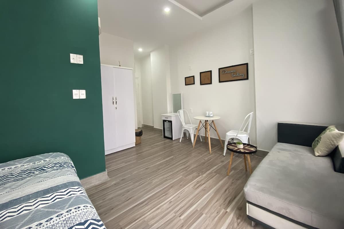 Quarto de hotel moderno com parede verde decorativa, um sofá, uma cama, uma mesa de jantar com cadeiras e uma pequena mesinha de apoio.