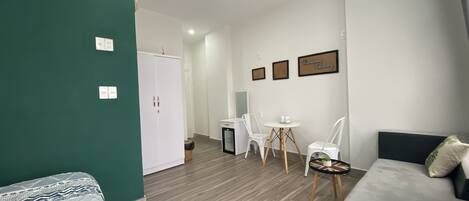 Una habitación de hotel moderna con una pared de acento verde, un sofá, una cama, una mesa de comedor con sillas y una mesita auxiliar.