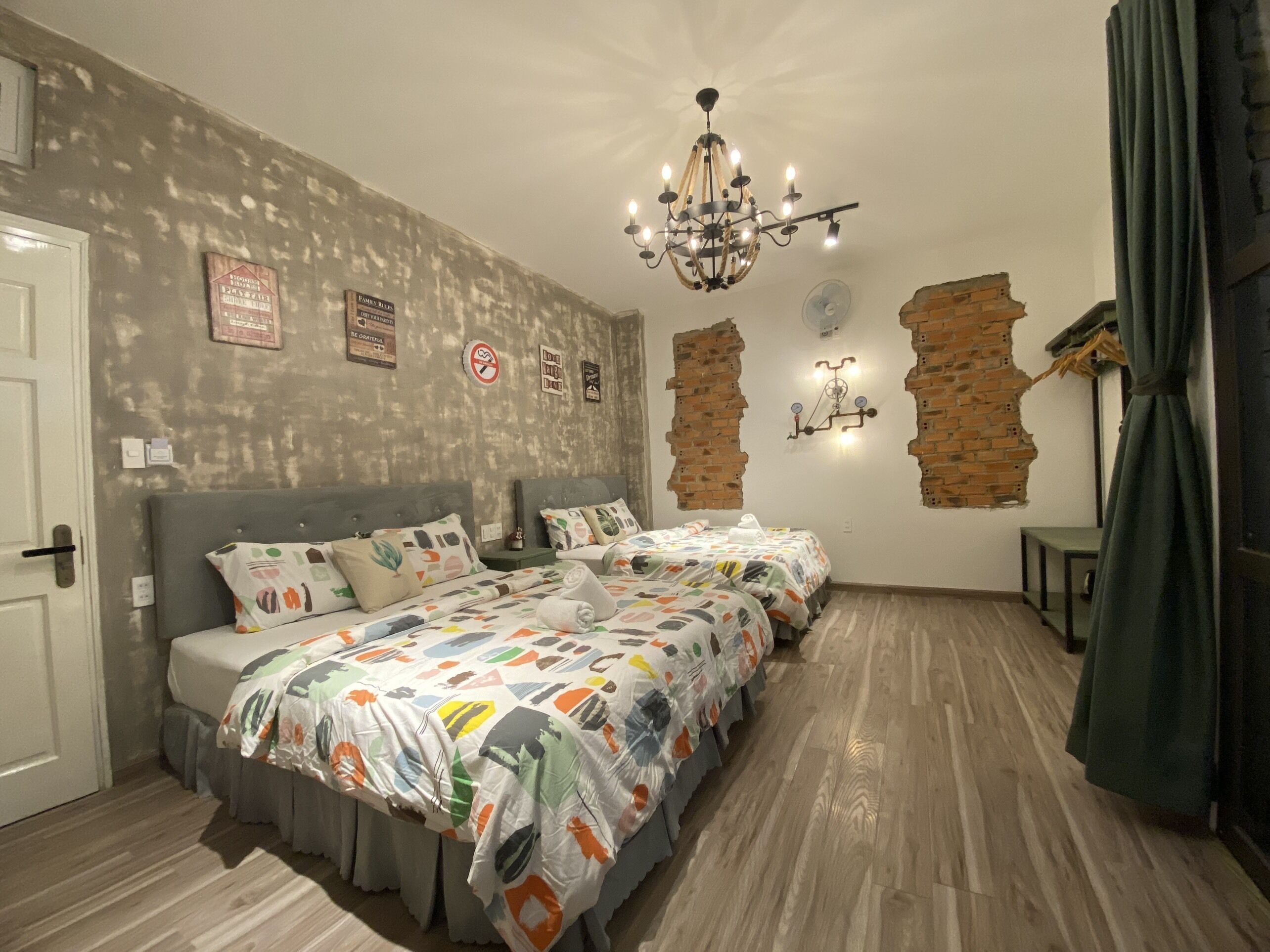 A room with two beds, a chandelier, and a brick wall feature.