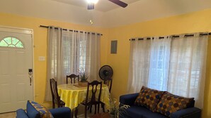 Un salon avec un mur jaune, une table à manger avec des chaises, un canapé bleu et un ventilateur.
