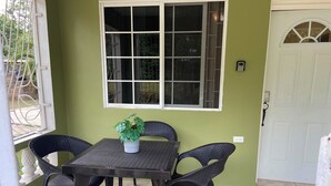 Une terrasse avec une table et quatre chaises, un pot de fleurs, une fenêtre avec des barreaux en métal et une porte blanche.