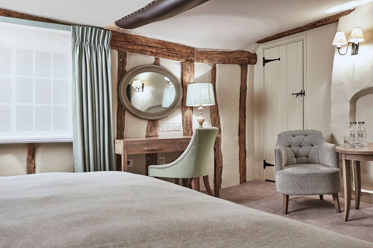 A bedroom with a bed, a desk, a chair, a mirror, and a lamp.