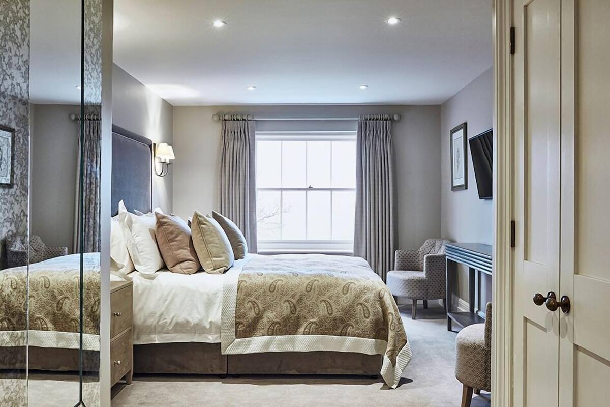 A bedroom with a large bed, a desk, and a chair, with a window and curtains.
