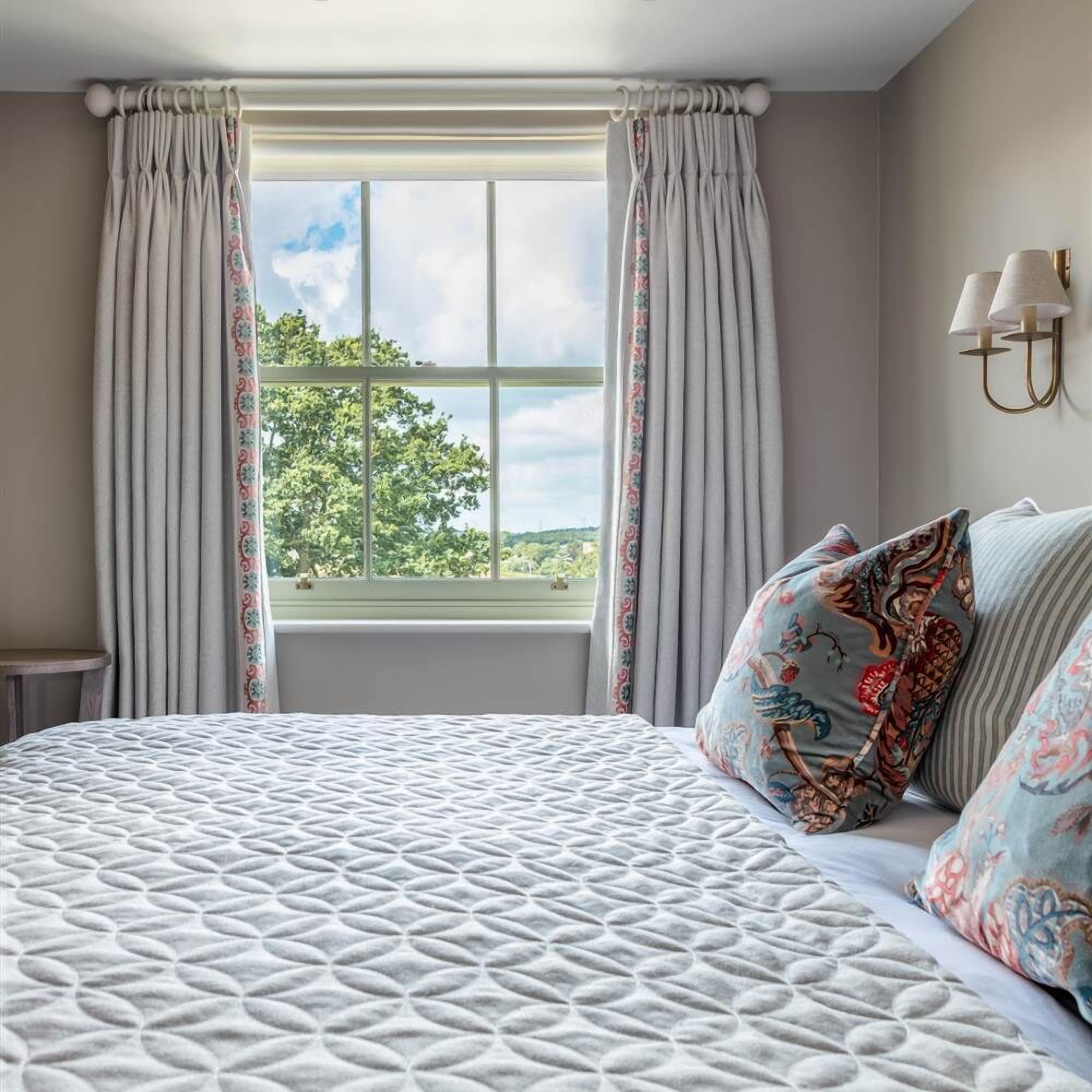 A bedroom with a large bed, a window with curtains, and a view of trees.