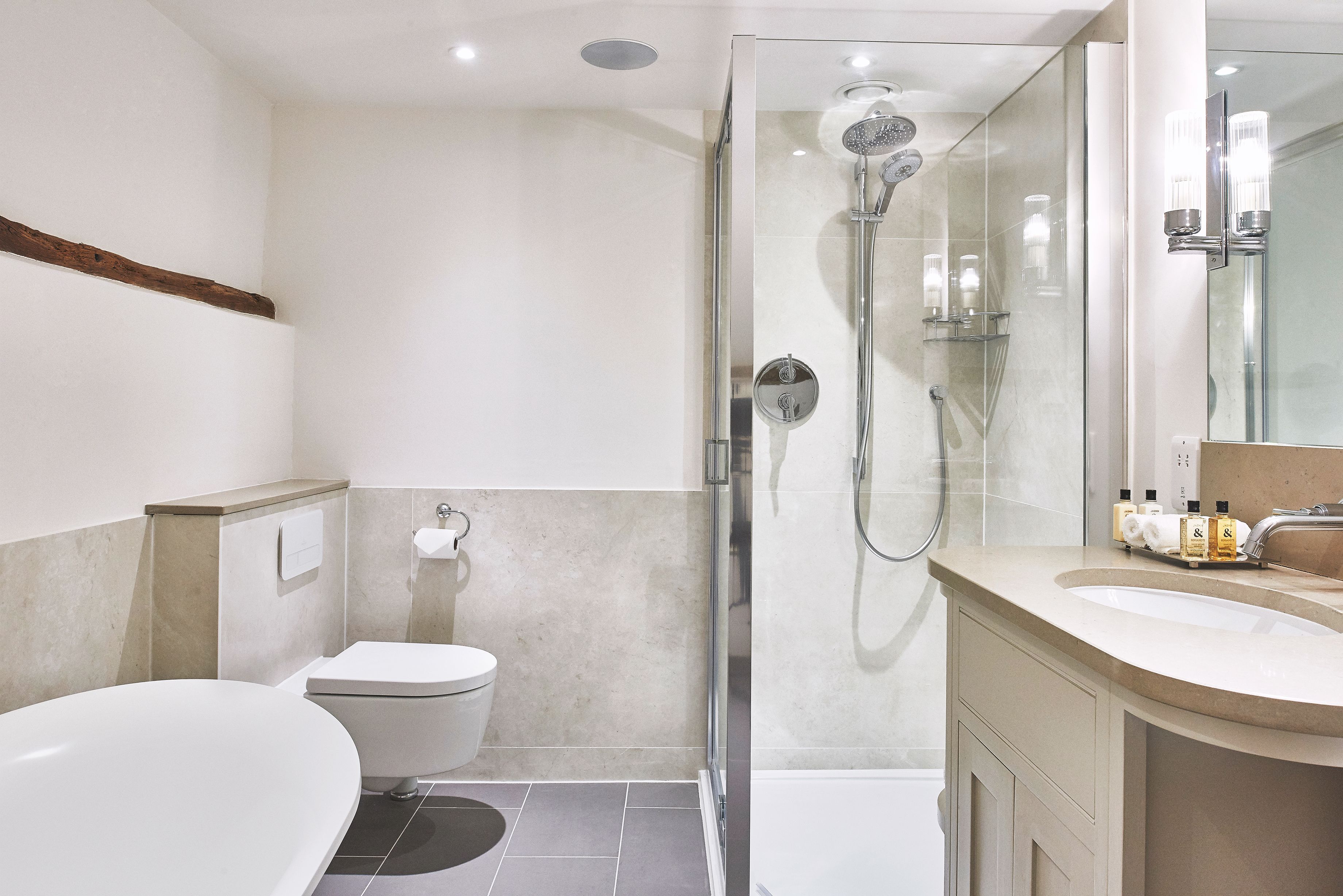 Un baño moderno con ducha envuelta en vidrio, una bañera independiente y un lavamanos con espejo.