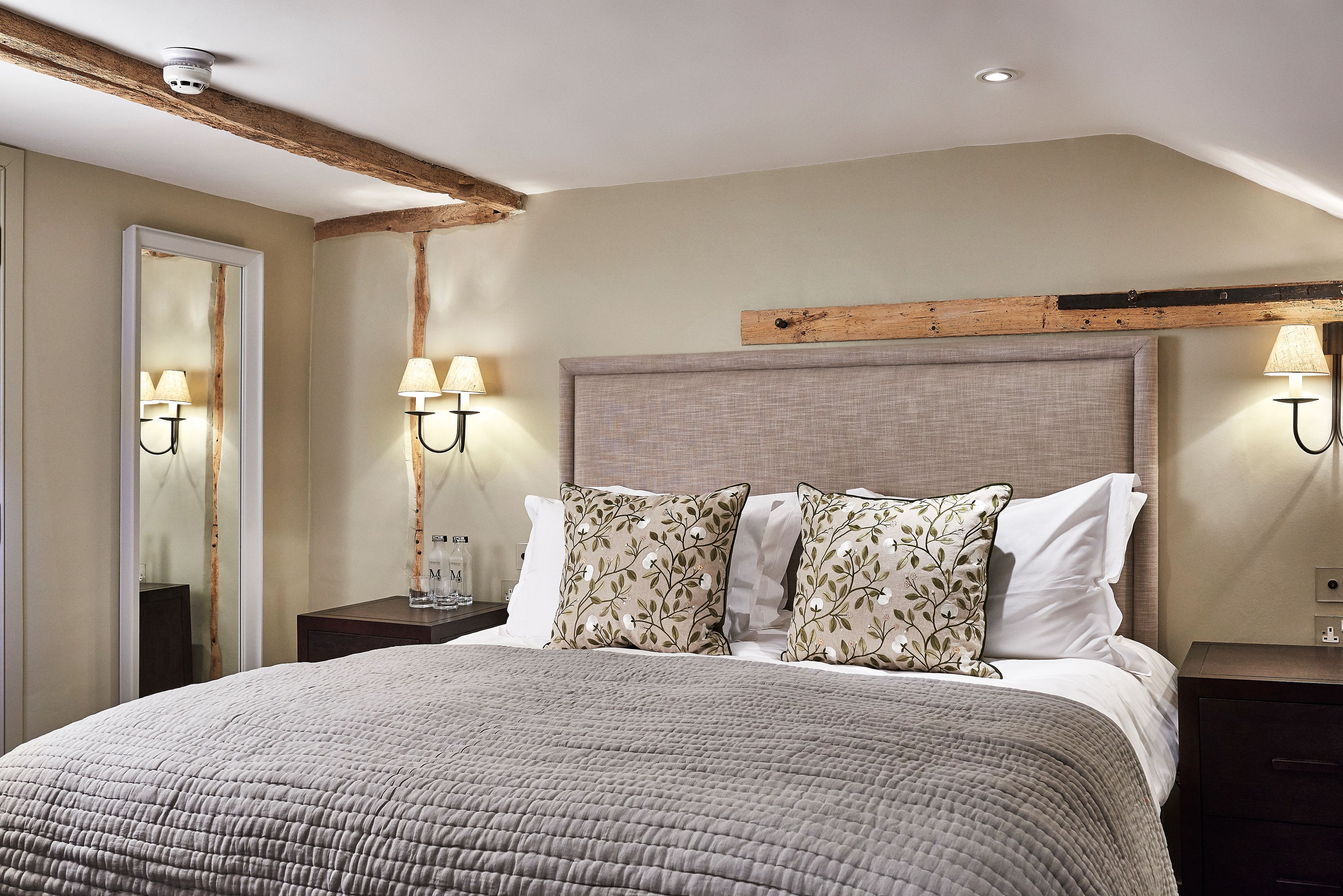 A bedroom with a large bed, two nightstands, a mirror, and wall-mounted lamps.