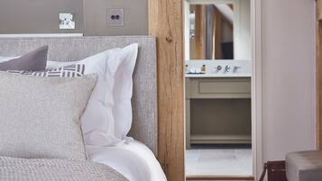 A neatly made bed with white and patterned pillows, a wooden headboard, and a view into a bathroom with a mirror and sink.
