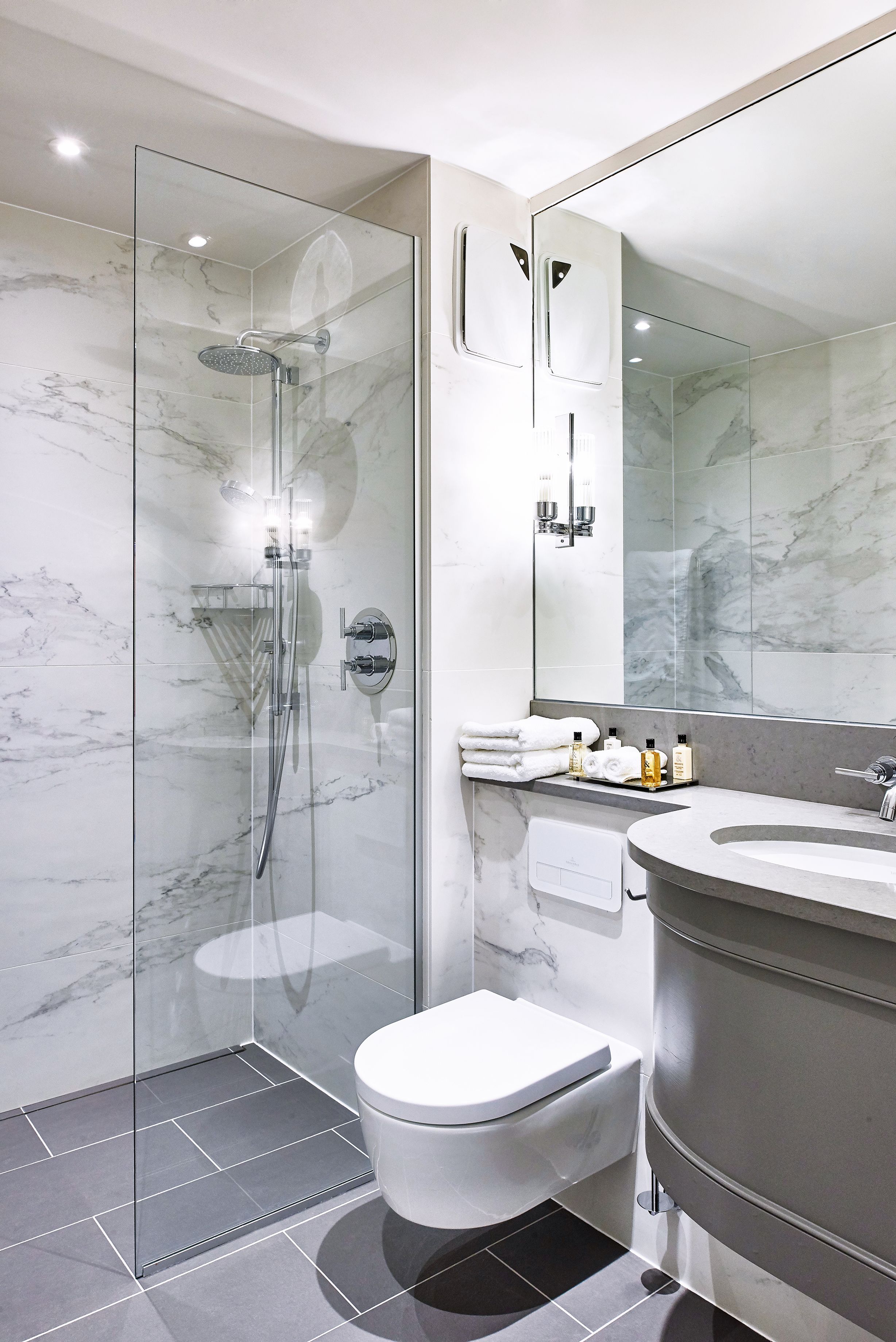 A modern bathroom with a glass-enclosed shower, a white toilet, and a marble-tiled sink area.