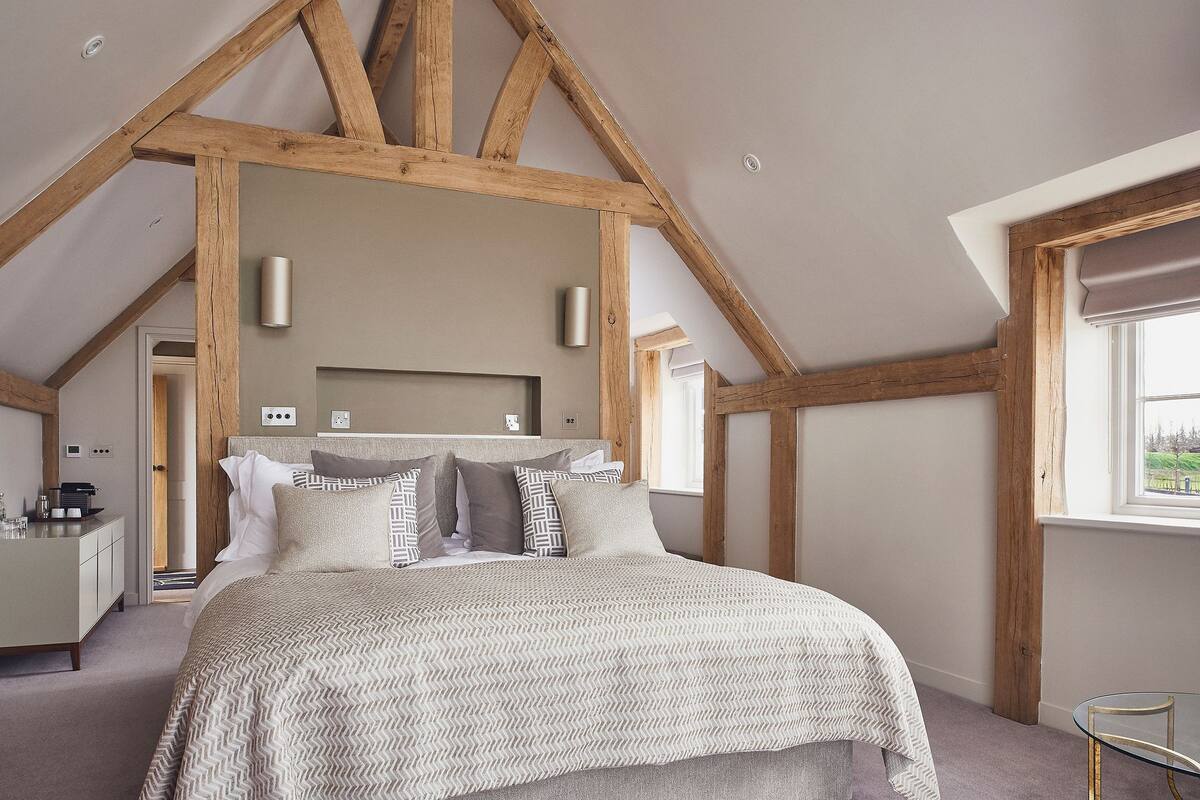 A bedroom with a bed, wooden beams, a headboard, bedside tables, and a window.
