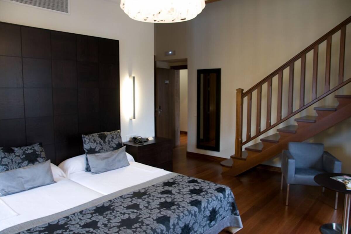 A bedroom with a large bed, a wooden staircase, and a small seating area.