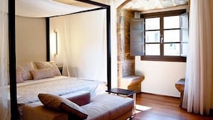 Un dormitorio con una cama con dosel, una mesita pequeña y una ventana con arco de piedra.