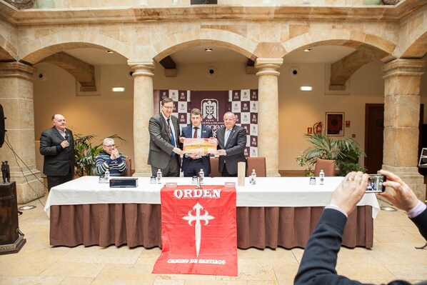 Evento formal con una mesa cubierta por un mantel, un cartel con texto y un atril para micrófono.