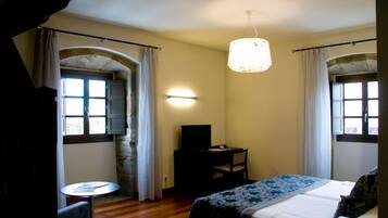 A hotel room with a bed, a desk with a chair, a small table, and a television.