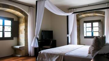 A bedroom with a bed, a television, stone walls, and a stone bench.