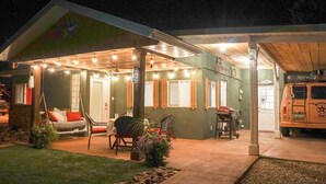 Un patio exterior acogedor con una silla mecedora, una mesa de comedor y una zona de estar cubierta con luces colgantes.