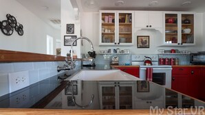 Una cocina moderna con una isla central, armarios blancos y detalles en rojo.