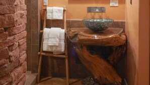 Un baño de diseño rústico, con una pared de piedra, un banco de madera con toallas, un espejo grande y un lavabo de madera.