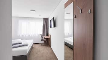 Habitación de hotel con cama, escritorio, silla y televisor montado en la pared.