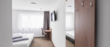 A hotel room with a bed, desk, chair, and a TV mounted on the wall.