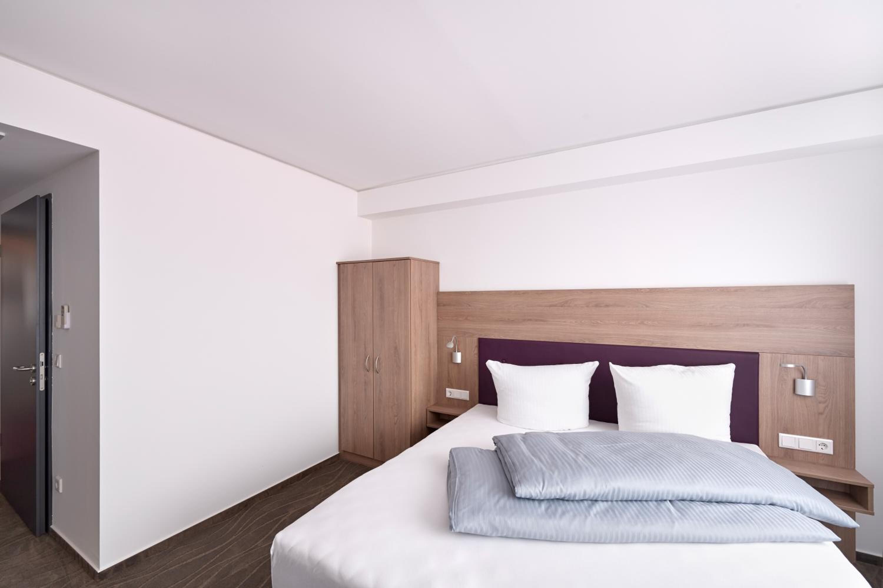 Ein modernes Hotelzimmer mit einem großen Bett, einem Holzschrank und einem Nachttisch mit Lampe.