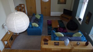Una sala de estar con un sofá azul, una mesa de centro de madera y un farol de papel blanco. Hay un cuadro en la pared y un televisor sobre un mueble.