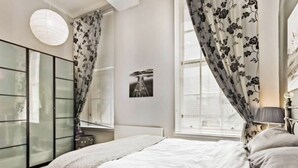 Un dormitorio con cama, armario, ventana con cortinas e imagen colgada en la pared.