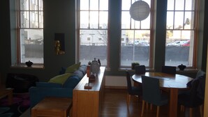 Una habitación con sofá, una mesa de comedor con sillas y ventanas grandes con persianas.