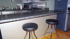Una cocina moderna con electrodomésticos de acero inoxidable, encimera de granito y dos taburetes de bar.
