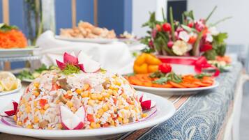 Una mesa con una ensalada grande de arroz y maíz como pieza central, rodeada de varios platos y un arreglo floral.
