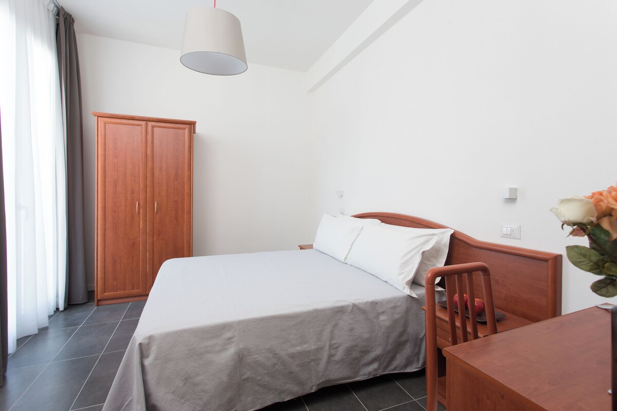 A bedroom with a bed, wooden wardrobe, and a desk with a chair.
