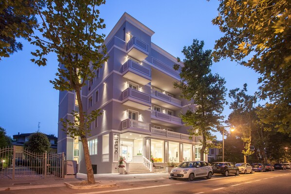 A multi-story hotel with balconies, a visible entrance, and a parking area with cars. - Hotel Star (Cesenatico)