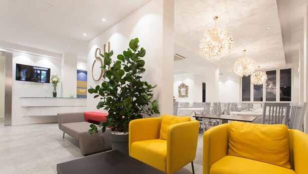 Una sala moderna con un sofá, un sillón amarillo, una mesa de centro y una planta grande en maceta.