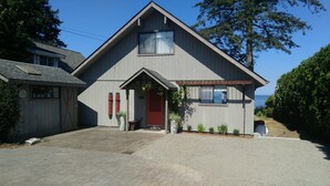 Una casa de dos pisos con una puerta roja, un porche pequeño y vista al mar.